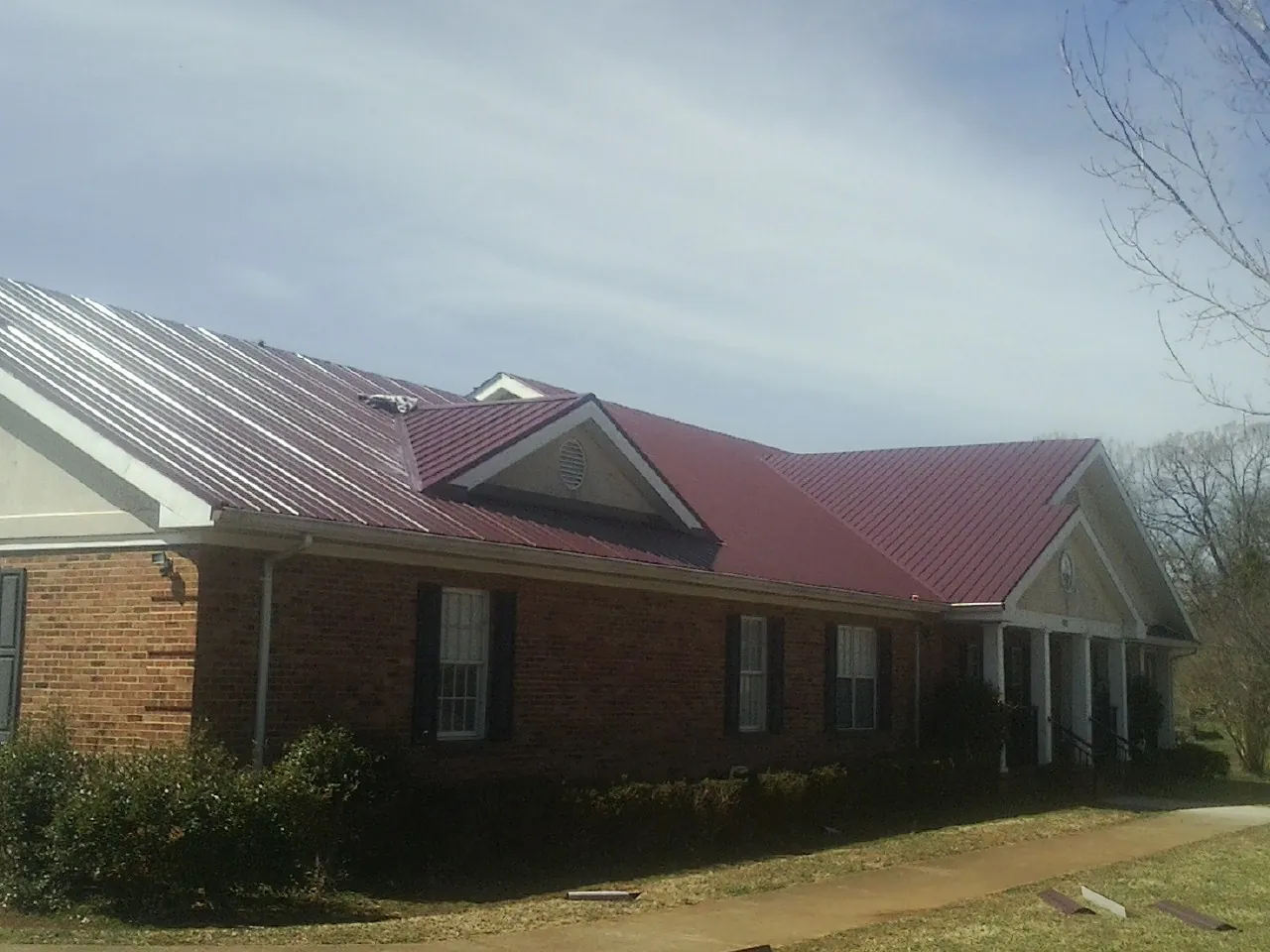 Red metal roof with gabled entries on a long brick building, from a Hail Damage Roof Repair job in Malone