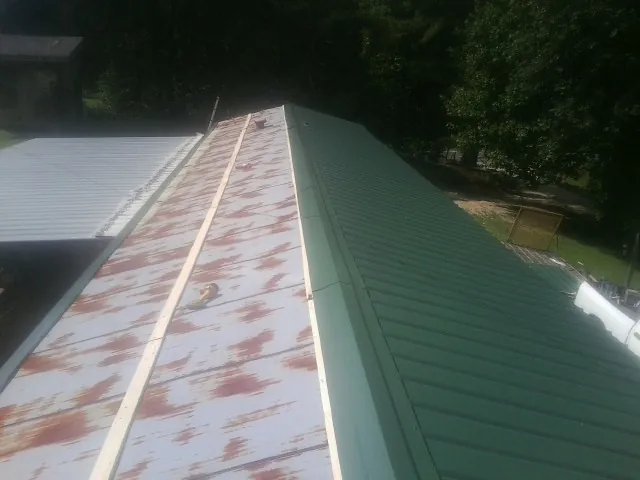 Old rusted panels beside newly installed green metal roofing — Wind Damage Roof Repair by Roofing Brothers in Malone