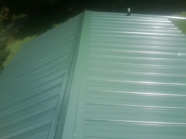 New green metal panels meeting at the ridge of a roof — Flat Roof Repair work by our crew in Malone
