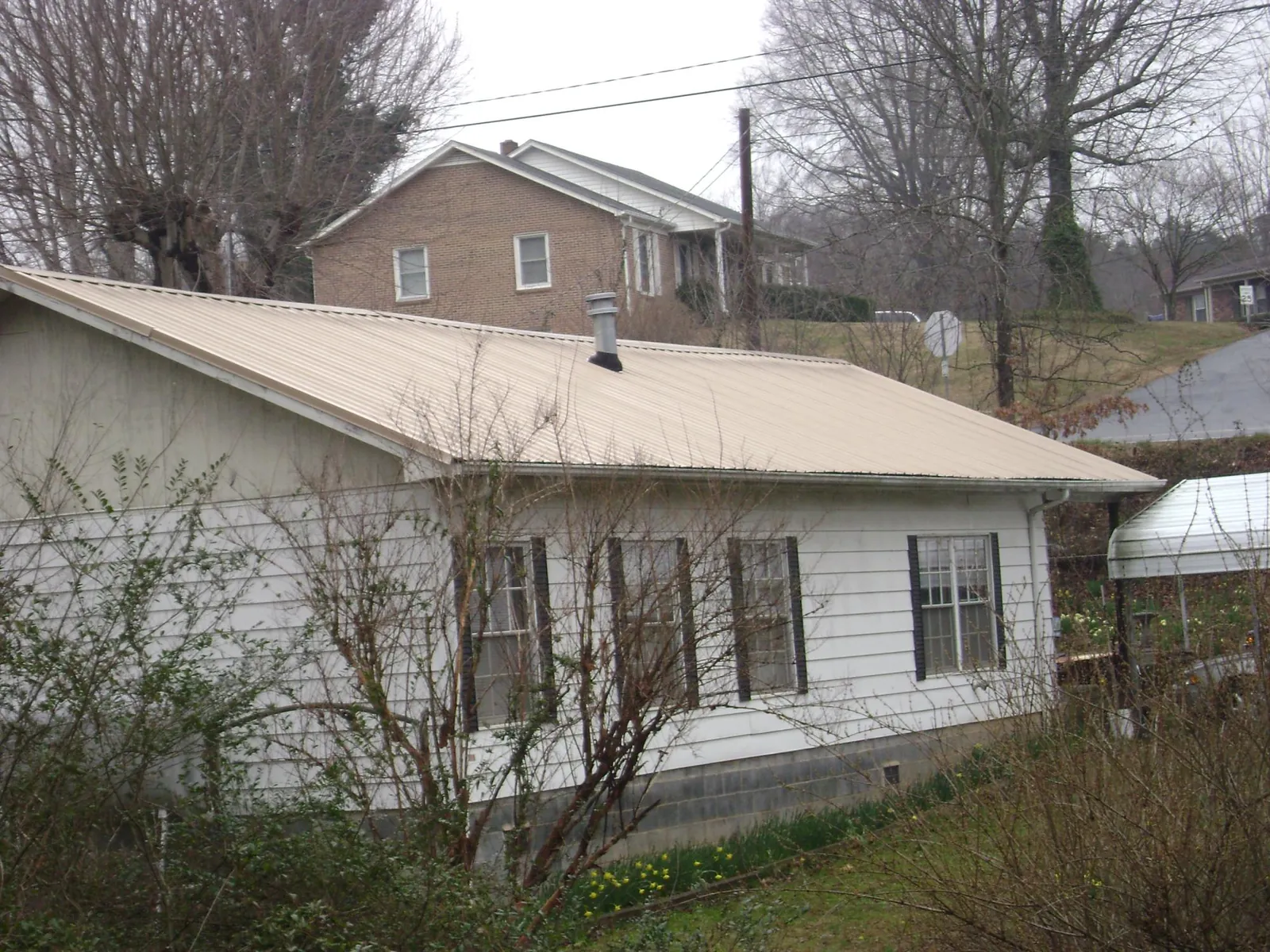 Tan metal roof on a white sided house set into a hillside — Commercial Roofing by Roofing Brothers in Malone
