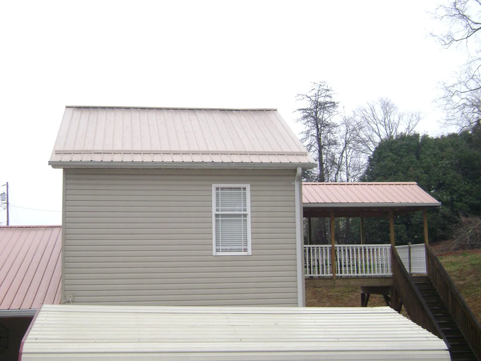 Tan metal roofs on a two story addition and attached porch, from a Roof Replacement job in Malone